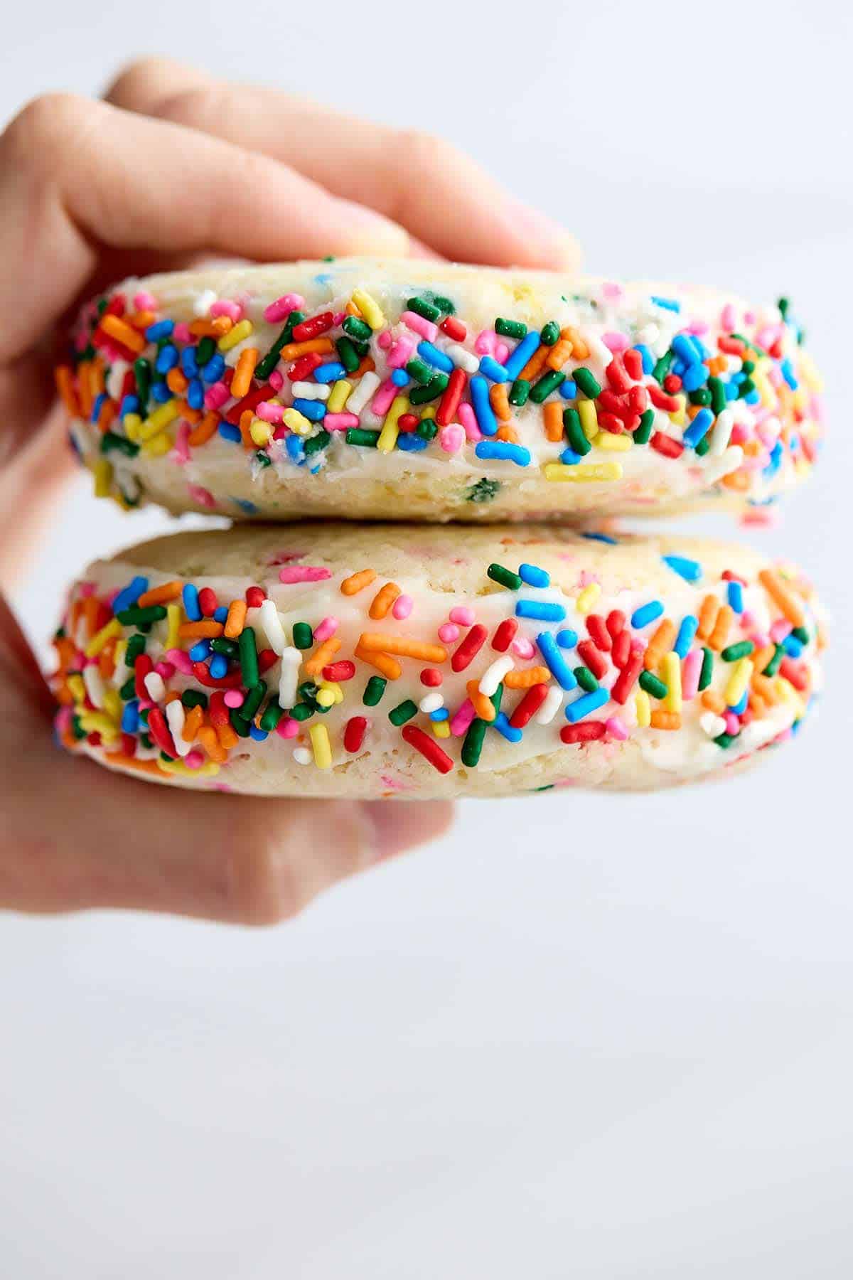 Fingers holding two colorful Funfetti cookie sandwiches so the sprinkle decorations are in view.