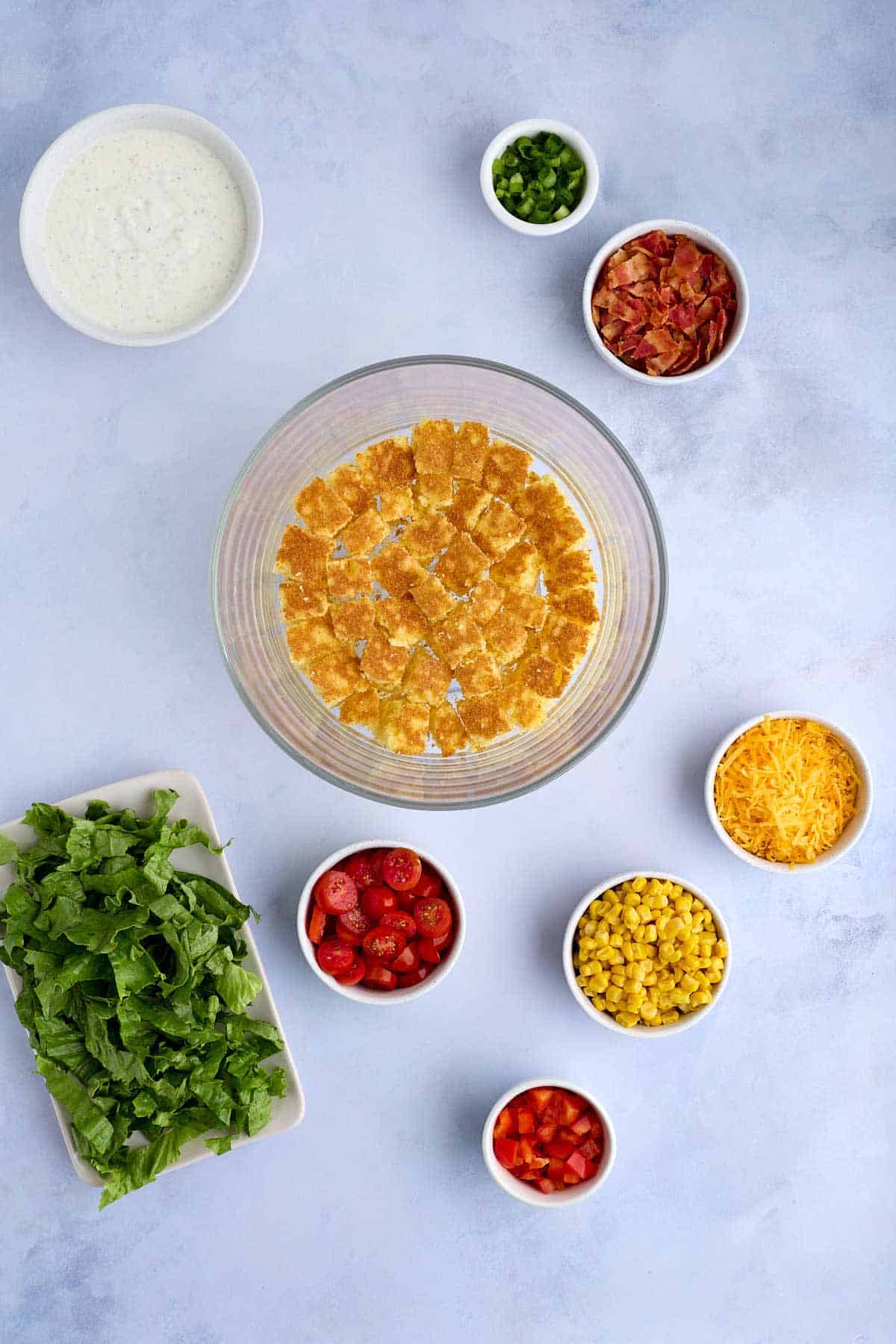 Layer of cornbread in a glass serving dish surrounded by all the rest of the ingredients that will be layered in the salad.