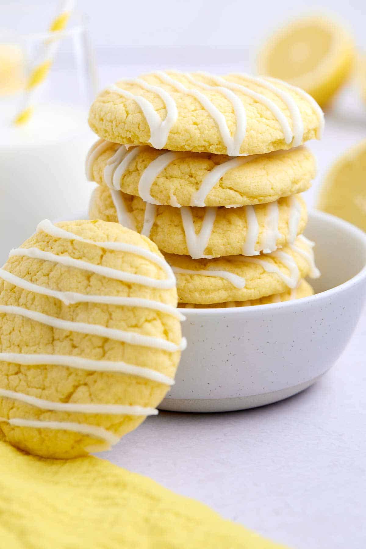Stack of lemon cake mix cookies in a bowl with one leaning against the bowl.