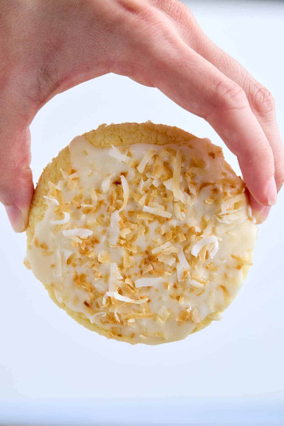 Fingers holding a pineapple cake mix cookie showing the size and the glaze with coconut.
