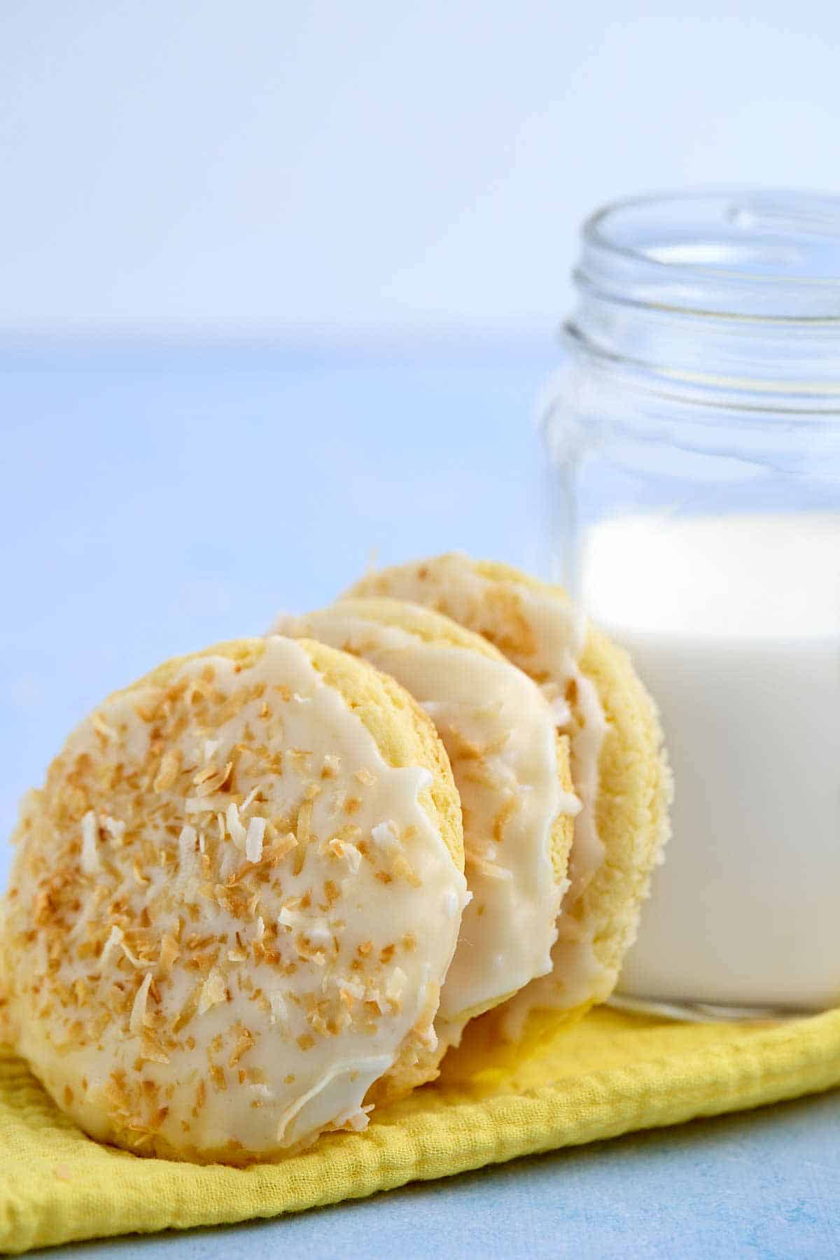 Three pineapple cookies leaning against a glass of milk.