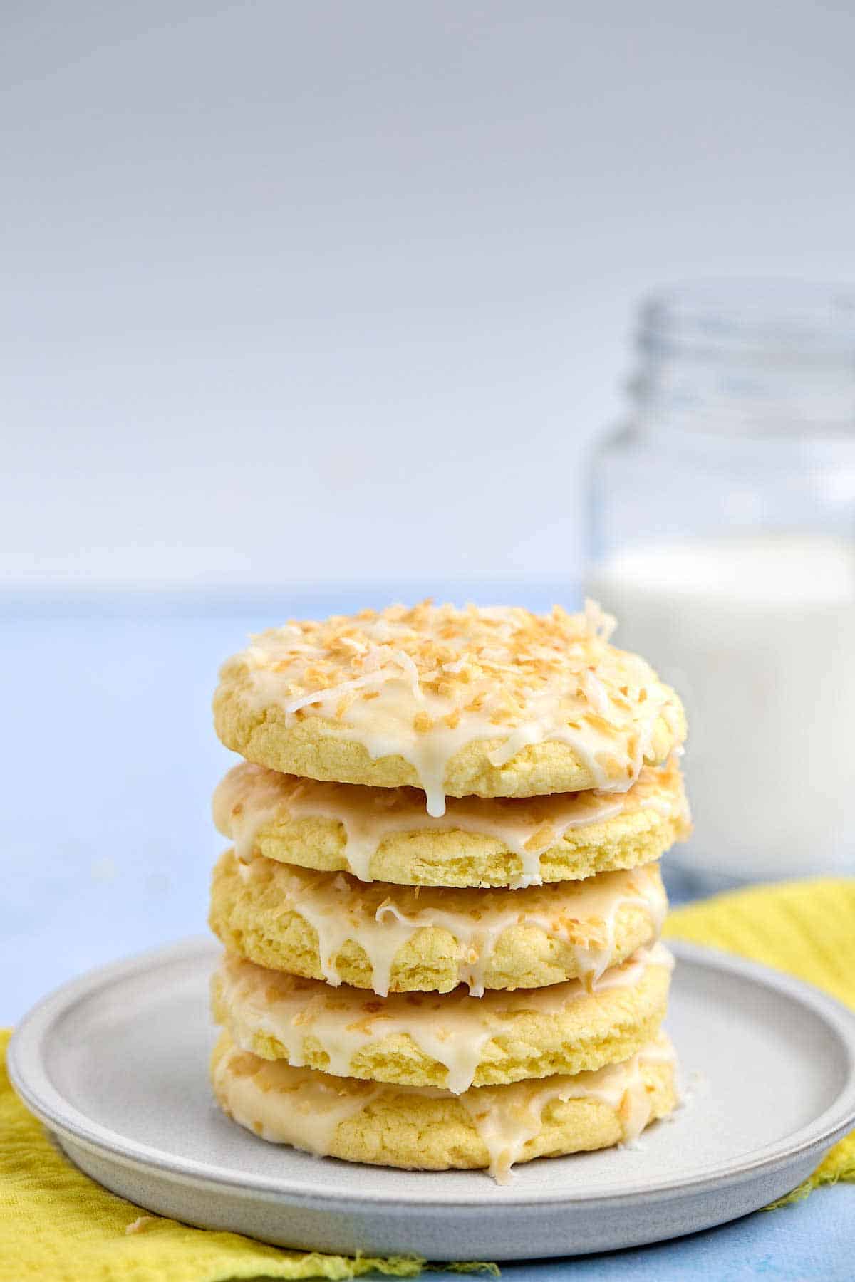 Stack of cookies on a plate with a glass of milk in the background.