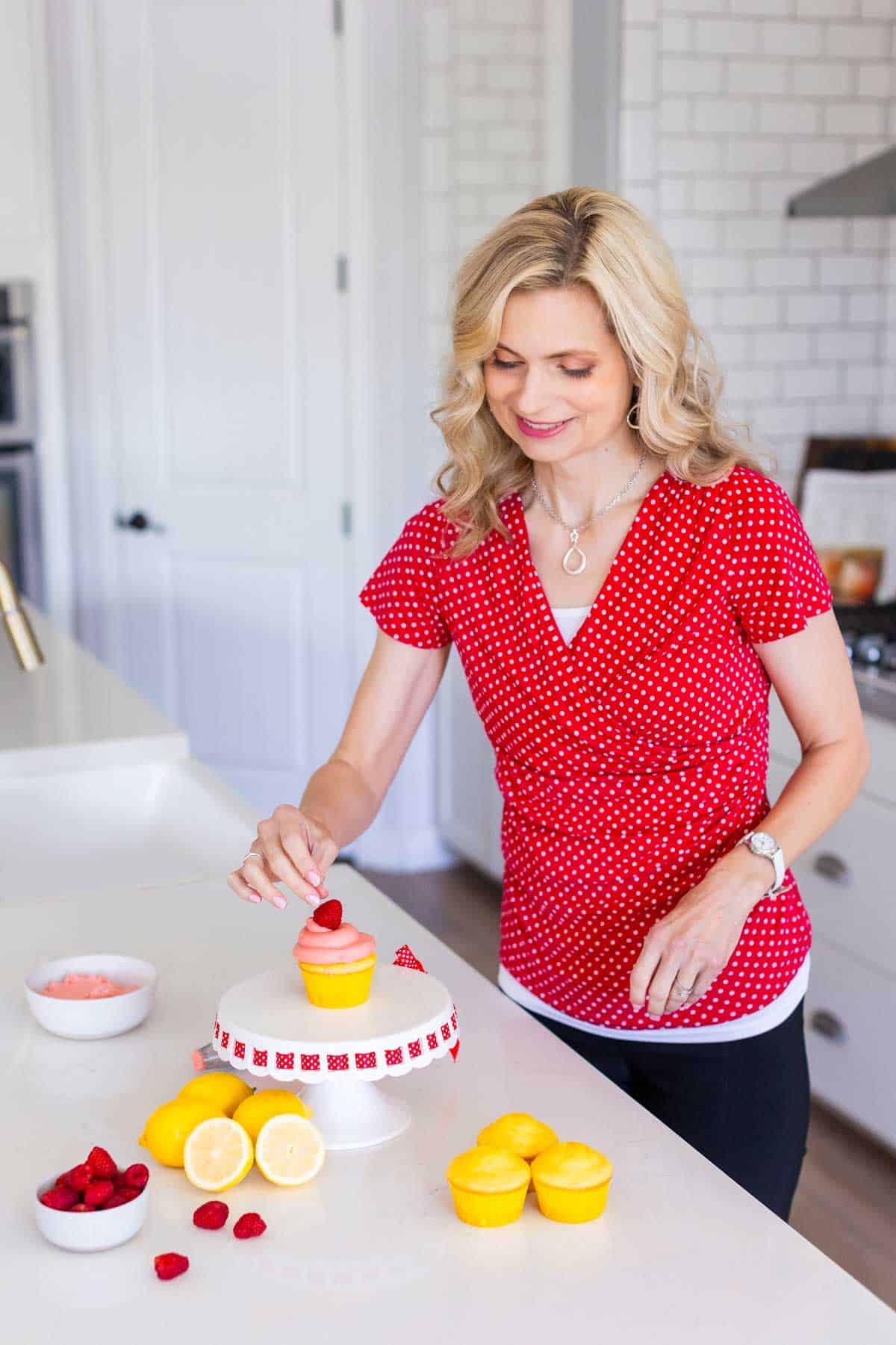 Woman decorating a lemon raspberry cupcake in a kitchen.