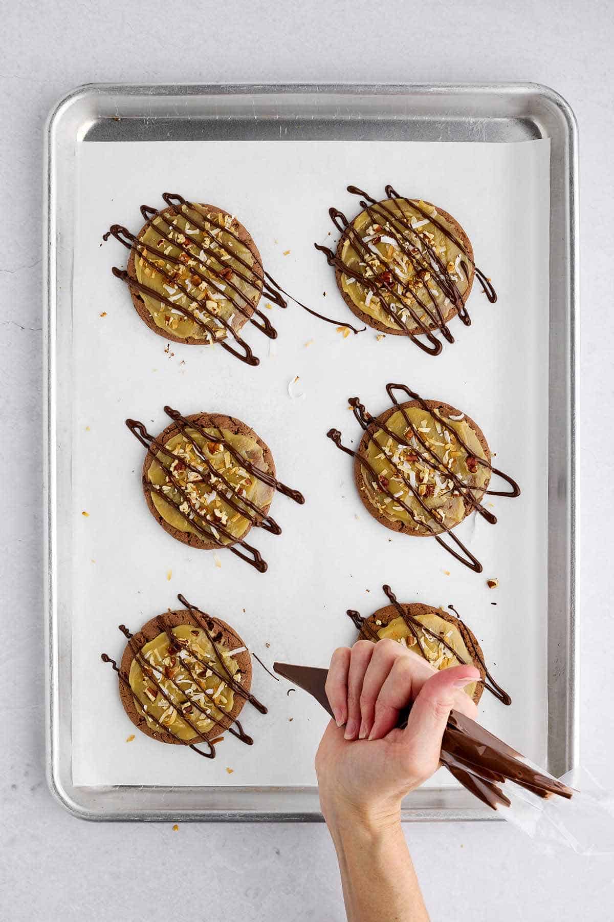 Hand drizzling chocolate on frosted German chocolate cake mix cookies.