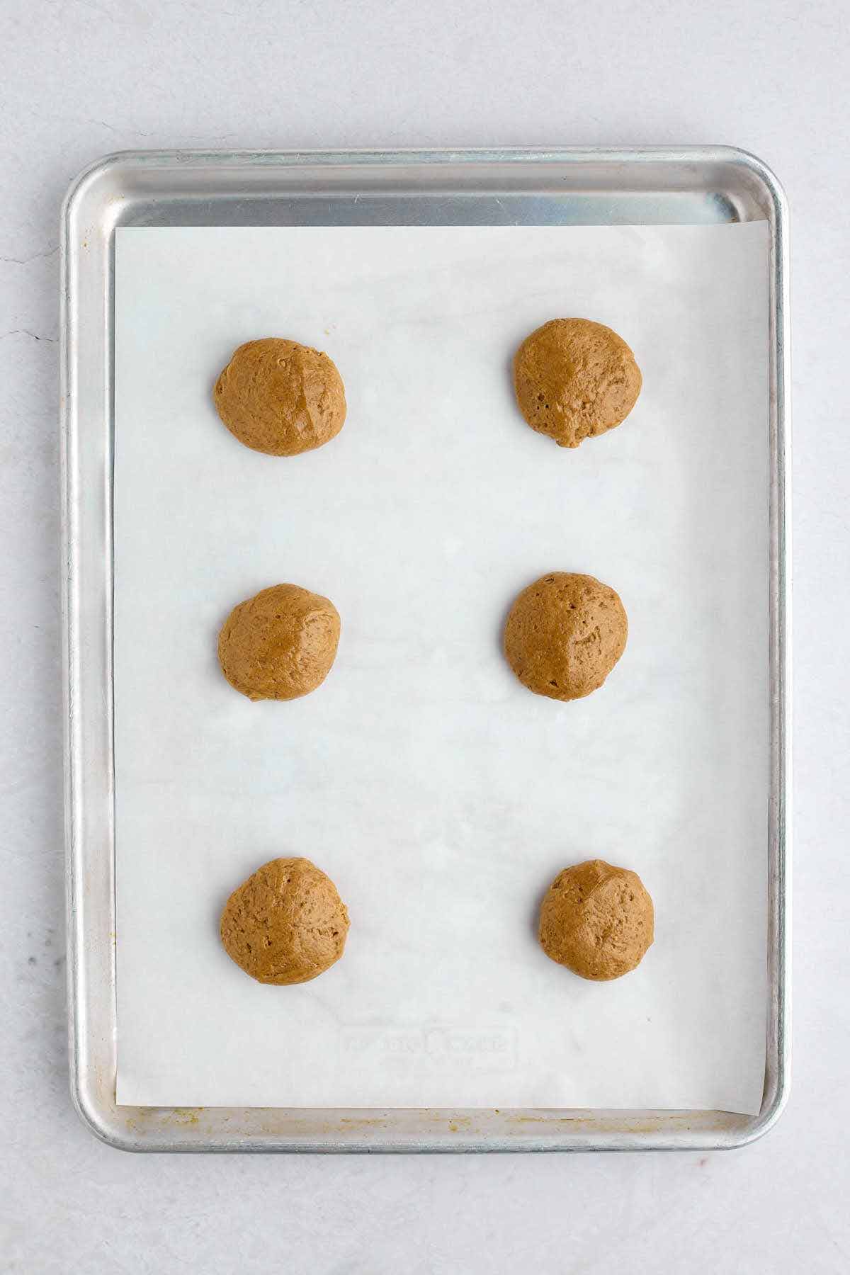 Cookie dough balls on a lined cookie sheet.
