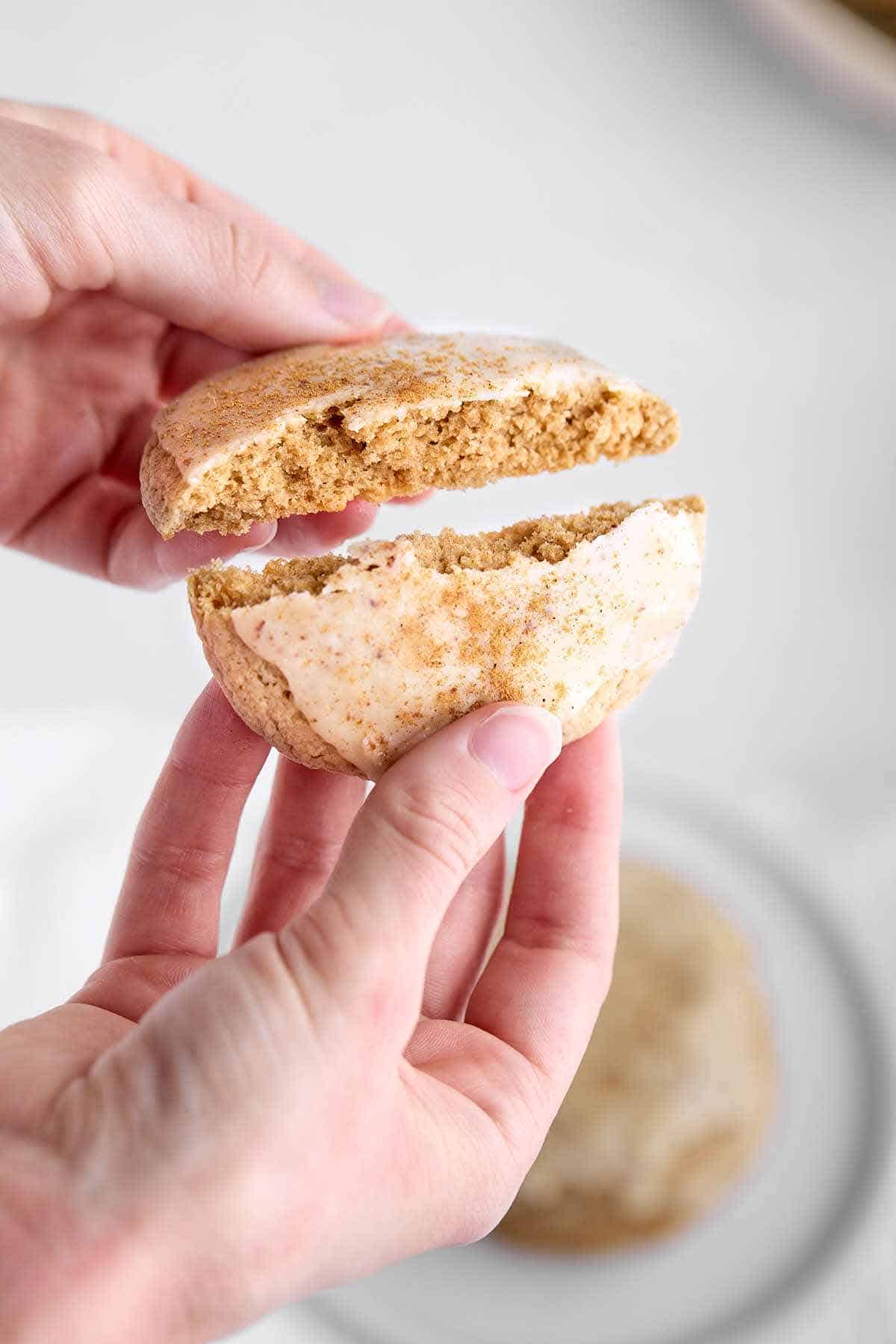 Fingers breaking a spice cookie in half to show the inside.