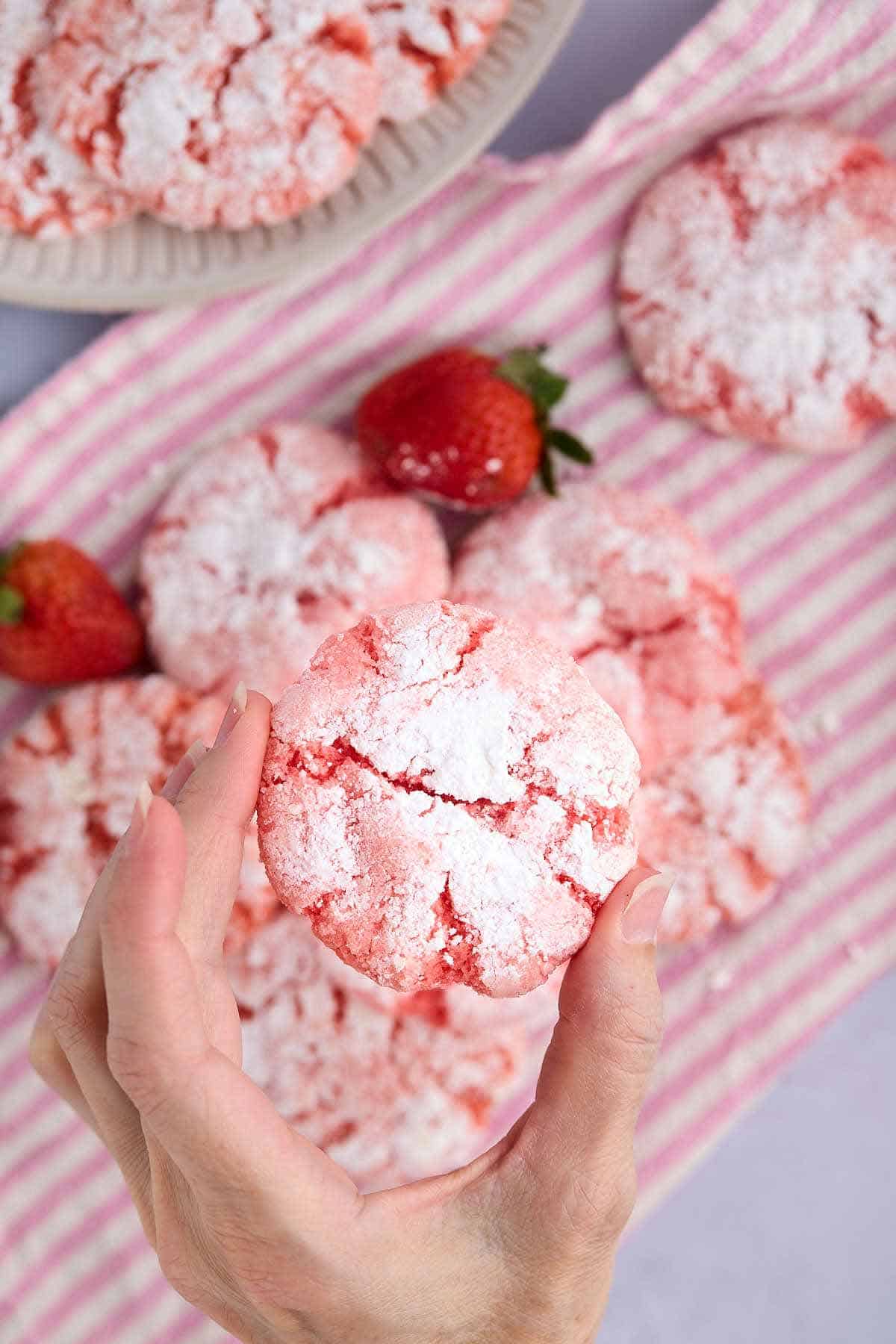 Overhead shot of fingers holding a strawberry crinkle cookie to show the size.
