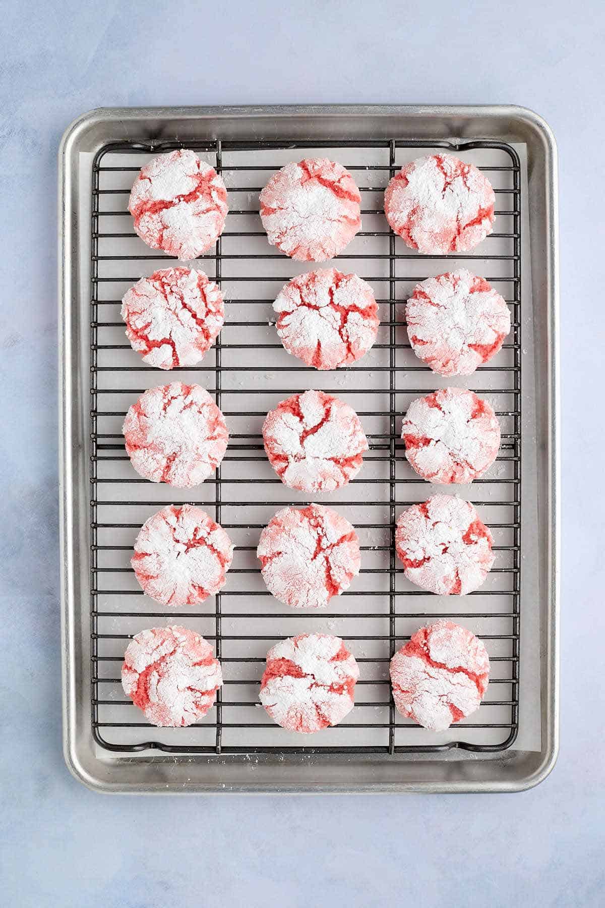 A cooling rack filled with baked strawberry crinkle cookies.