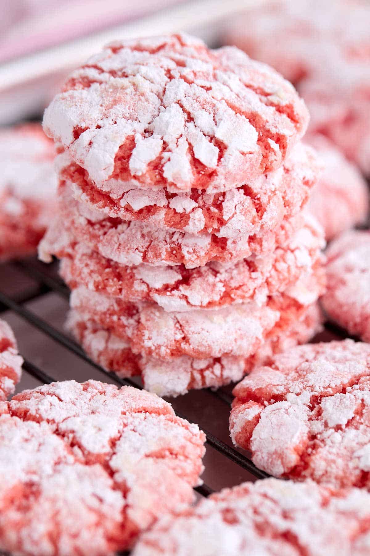 Stack of strawberry crinkle cookies on a cooling rack surrounded by other cookies.