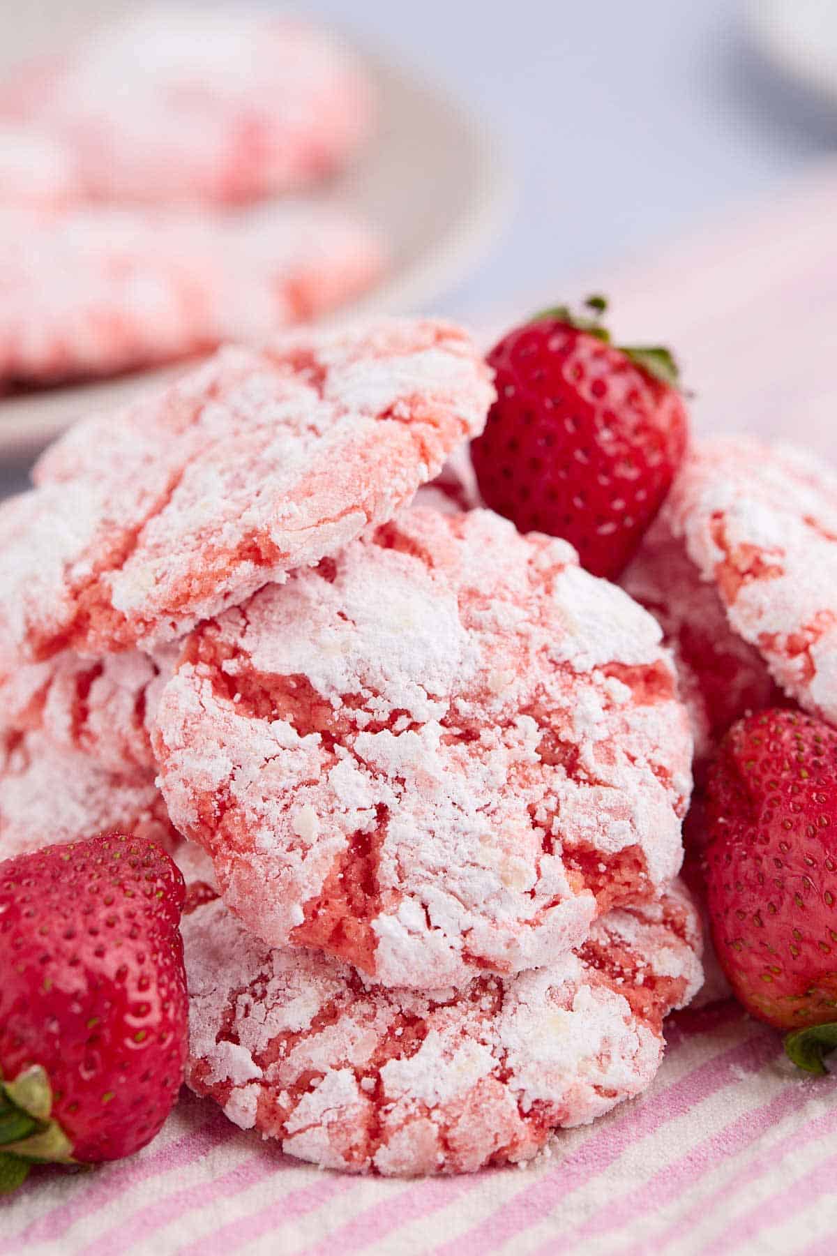 Stack of strawberry cake mix crinkle cookies with strawberries mixed in the pile.