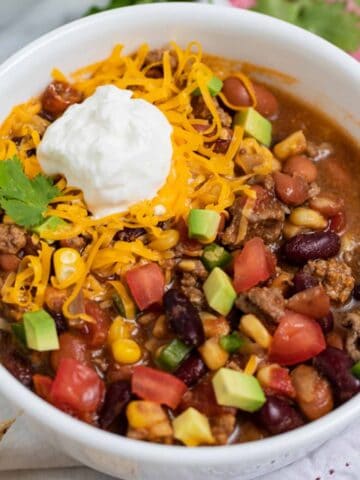 Bowl of slow cooker taco soup with ground beef garnished with sour cream and shredded cheese.