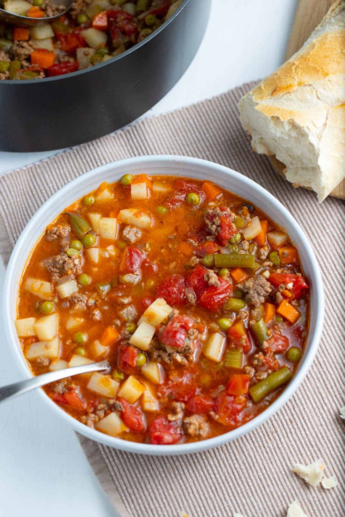 Overhead shot of vegetable ground beef soup with the soup pan and crusty bread in the background.