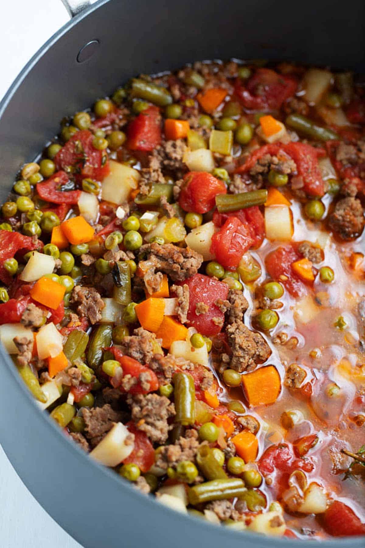Vegetable ground beef soup in a large pot on the stove.