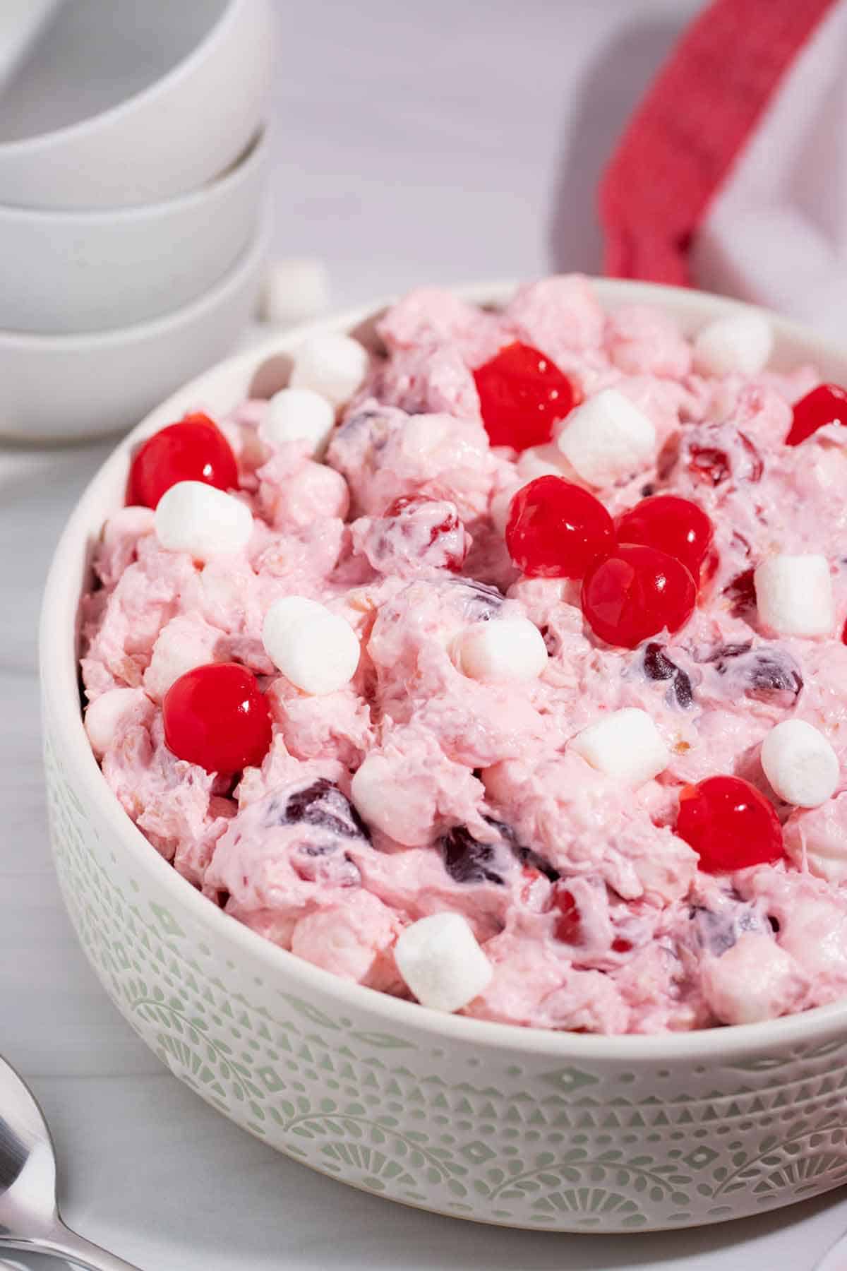 Large bowl of cherry fluff salad topped with marshmallows and cherries.