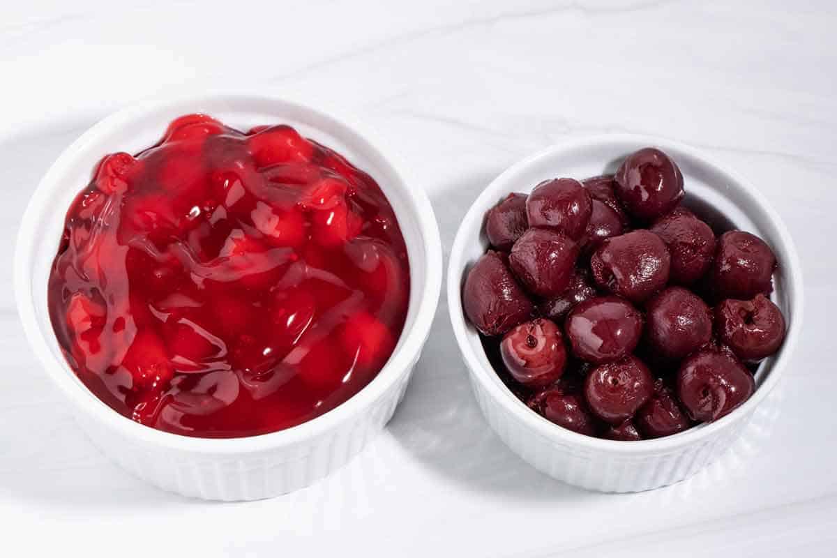 A bowl of cherry pie filling next to a bowl of canned cherries.