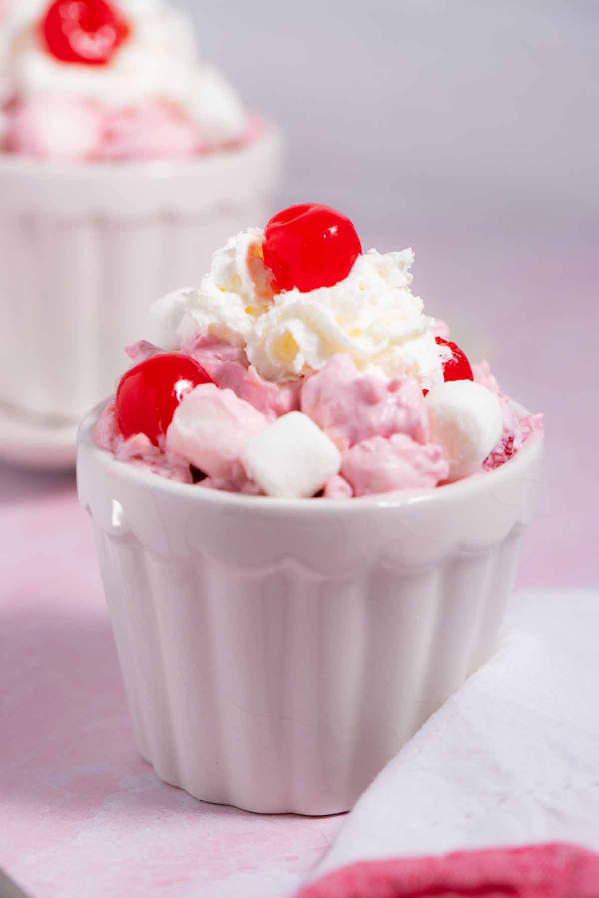 Small cup of cherry fluff salad with Cool Whip and a cherry on top.