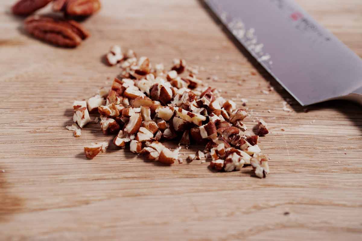 Pile of chopped pecans on a cutting board.