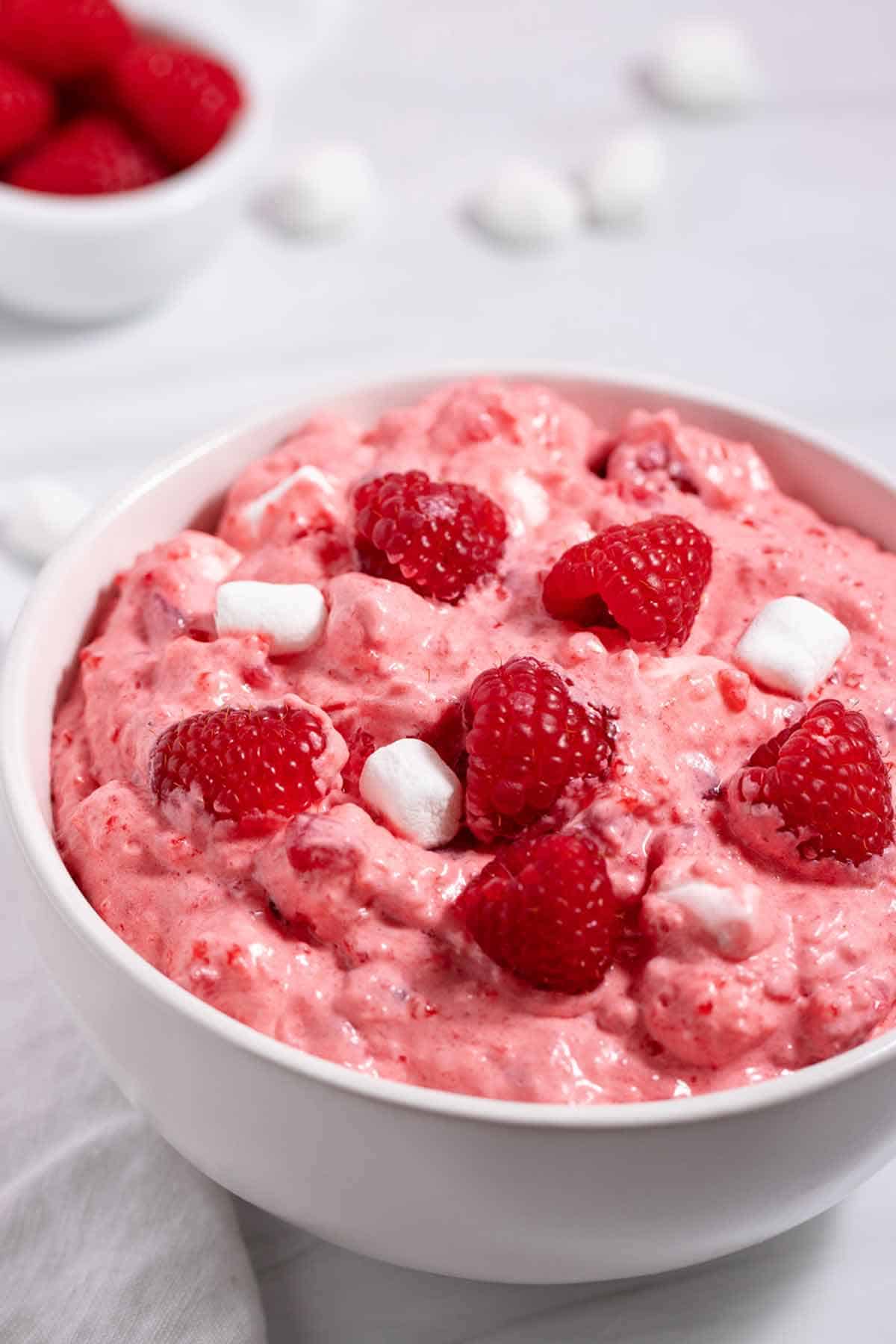Bowl of cranberry raspberry jello salad topped with fresh raspberries and marshmallows.