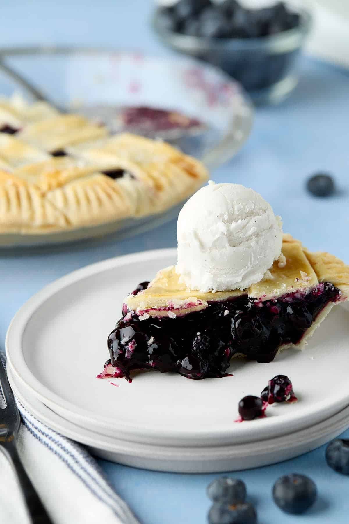 A plate with a slice of blueberry pie with a scoop of ice cream on top.