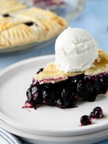 Slice of blueberry pie with canned filling with a scoop of ice cream on top.