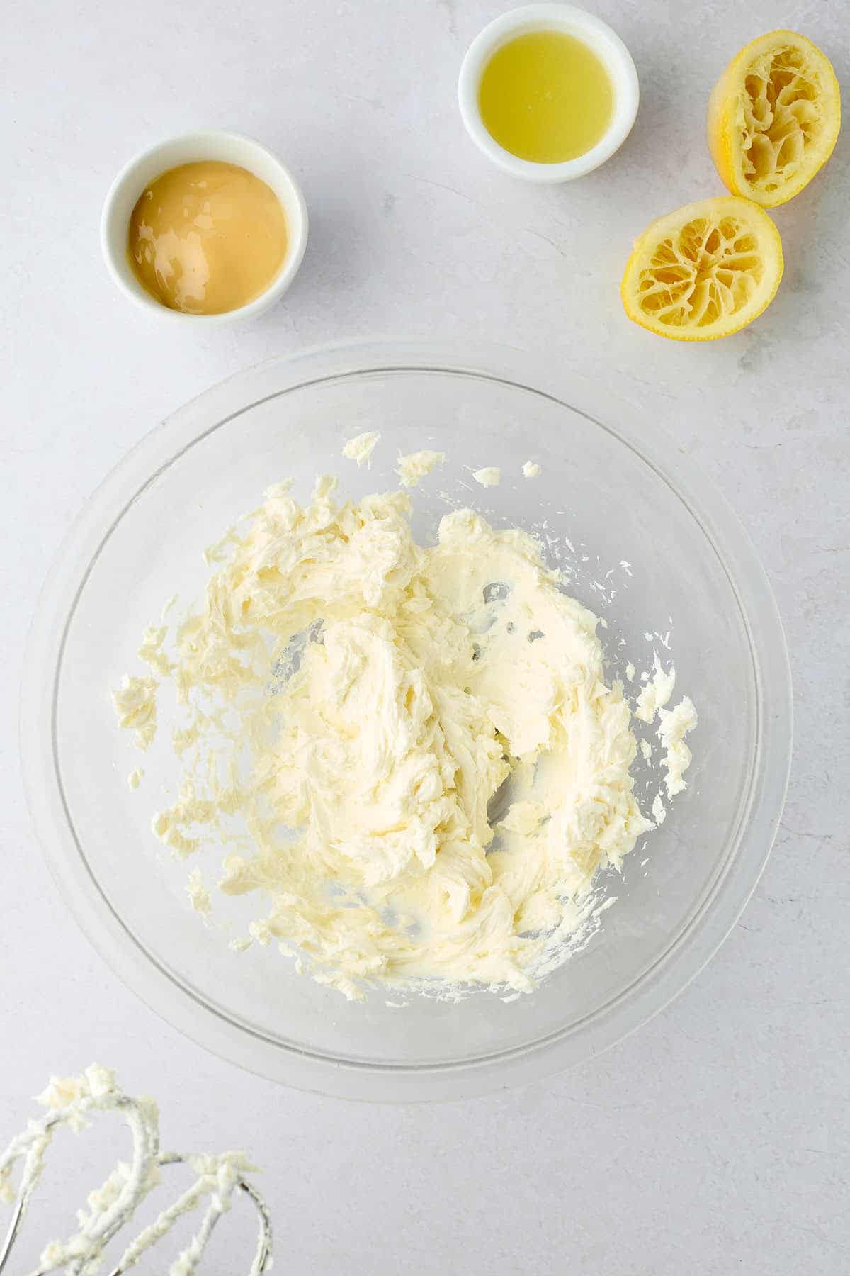 Softened cream cheese whipped in a bowl with lemon juice and sweetened condensed milk next to it.
