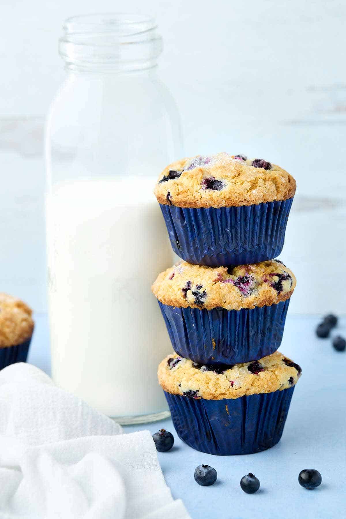 Stack of three blueberry buttermilk muffins next to a tall jug of milk.
